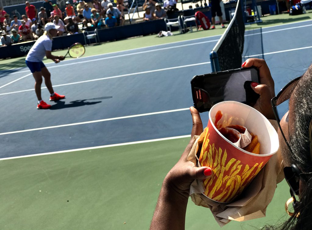 NEW YORK, NY - SEPTEMBER 08:  A spectator snaps a photo of Martina Navratilova while holding a bucket of fries during the women's Championship Doubles Semifinals on a 90+ degree day.  Martina Navratilova and Arantxa Sánchez Vicario defeated Tracy Austin and Gigi Fernandez. Day Eleven of the 2016 US Open at the USTA Billie Jean King National Tennis Center on September 8, 2016 in Queens.  (Landon Nordeman for ESPN)